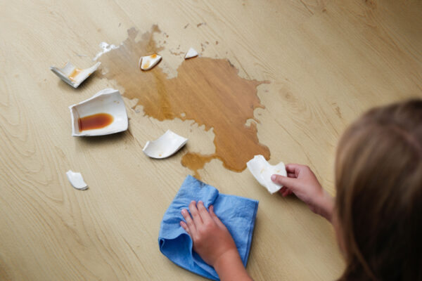 A broken cup of coffee fell on laminate, coffee spilled on floor.